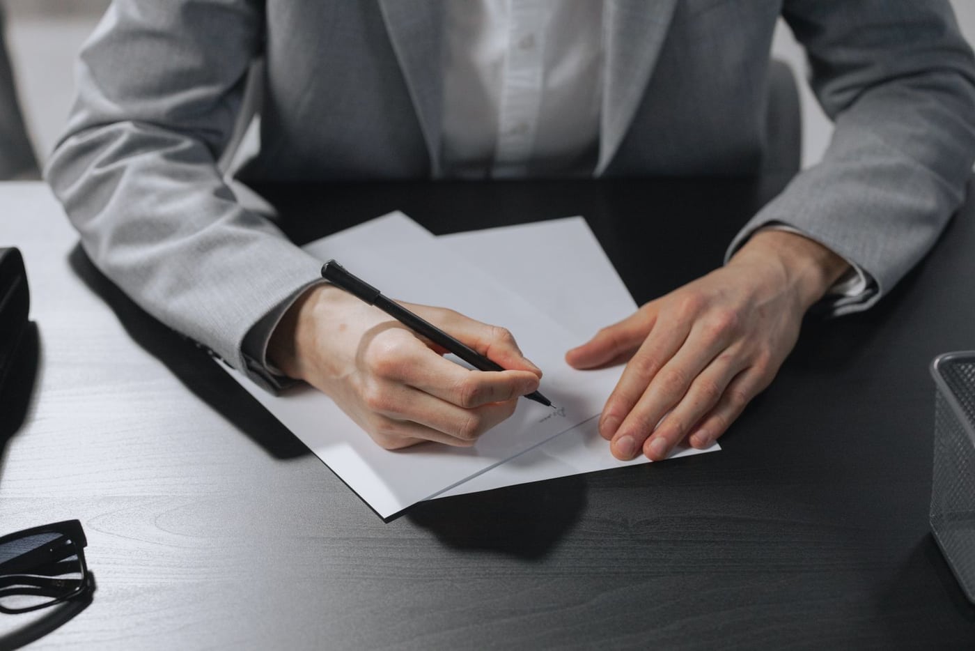 A person in a grey suit signing paperwork with a black pen
