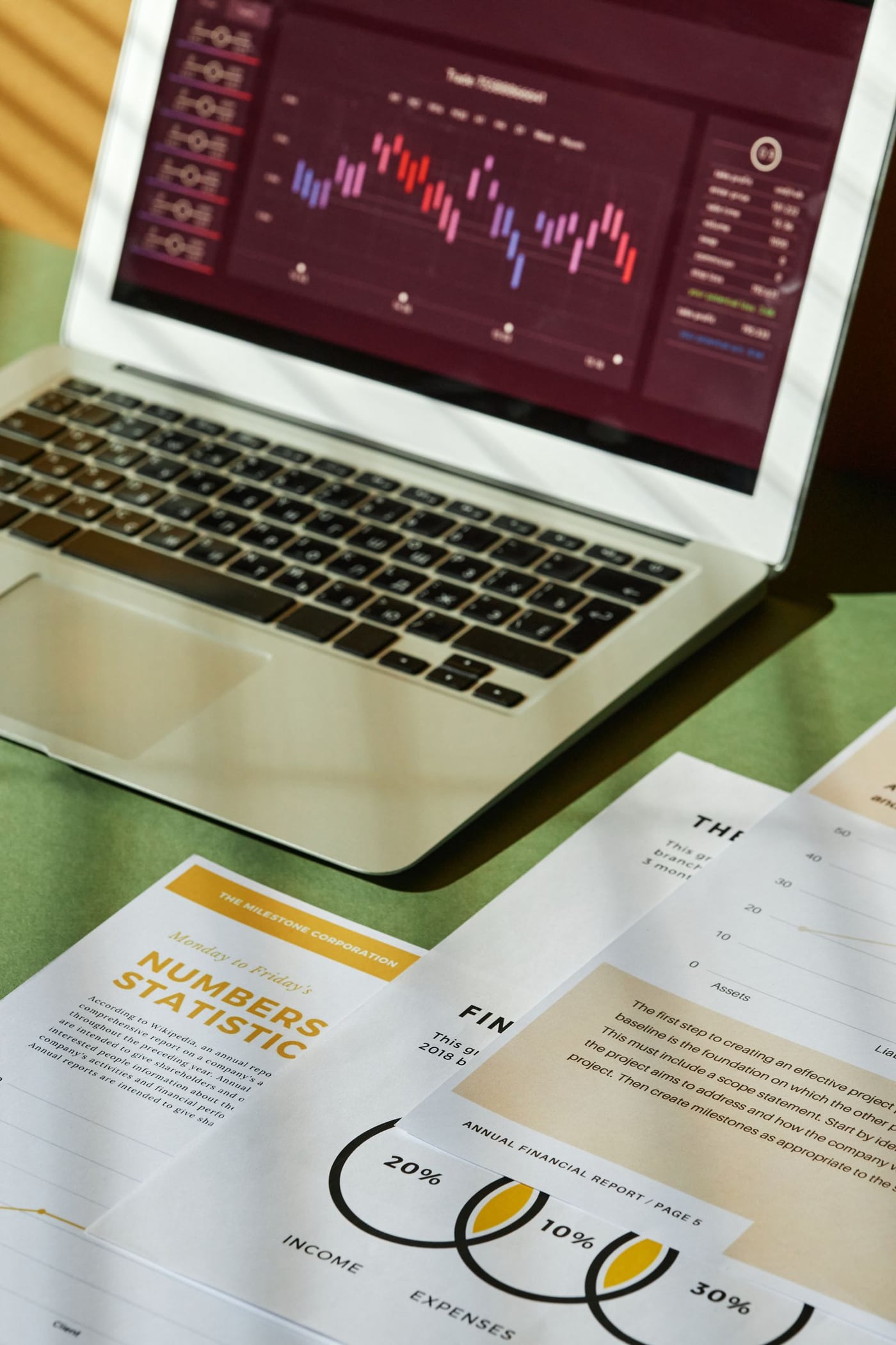 Financial reports beside a laptop displaying charts