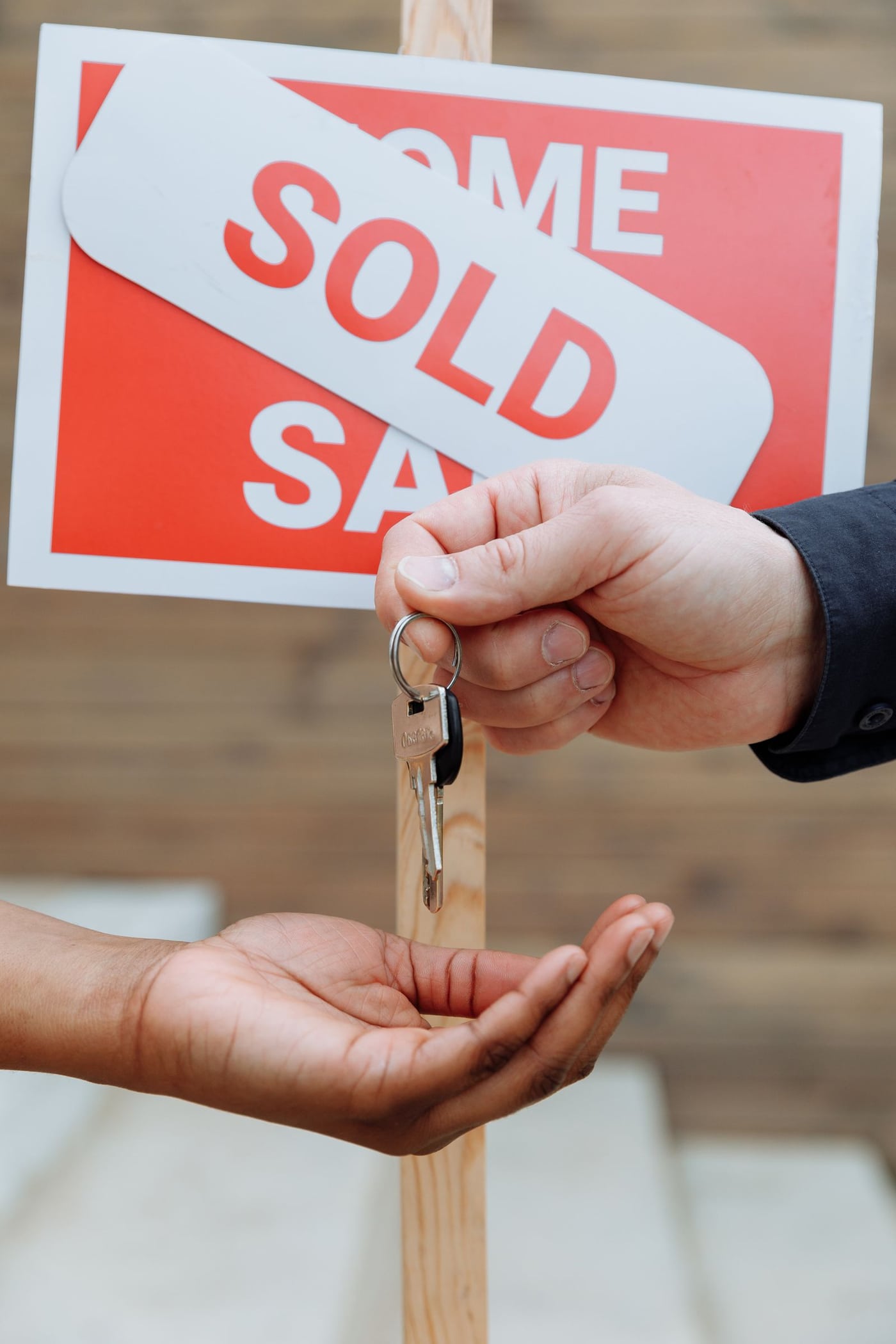 Hands exchanging house keys in front of a sold sign