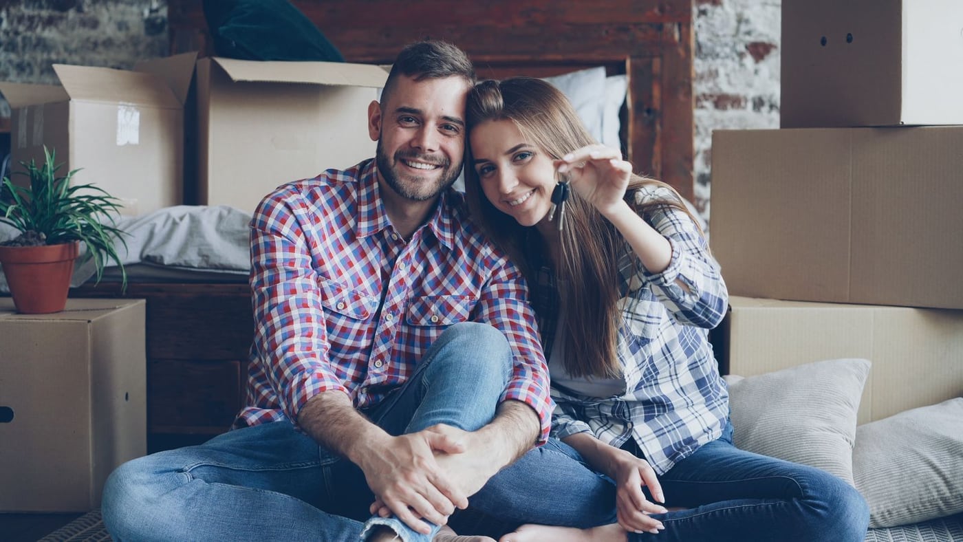 Couple holding house keys beside moving boxes in their new home